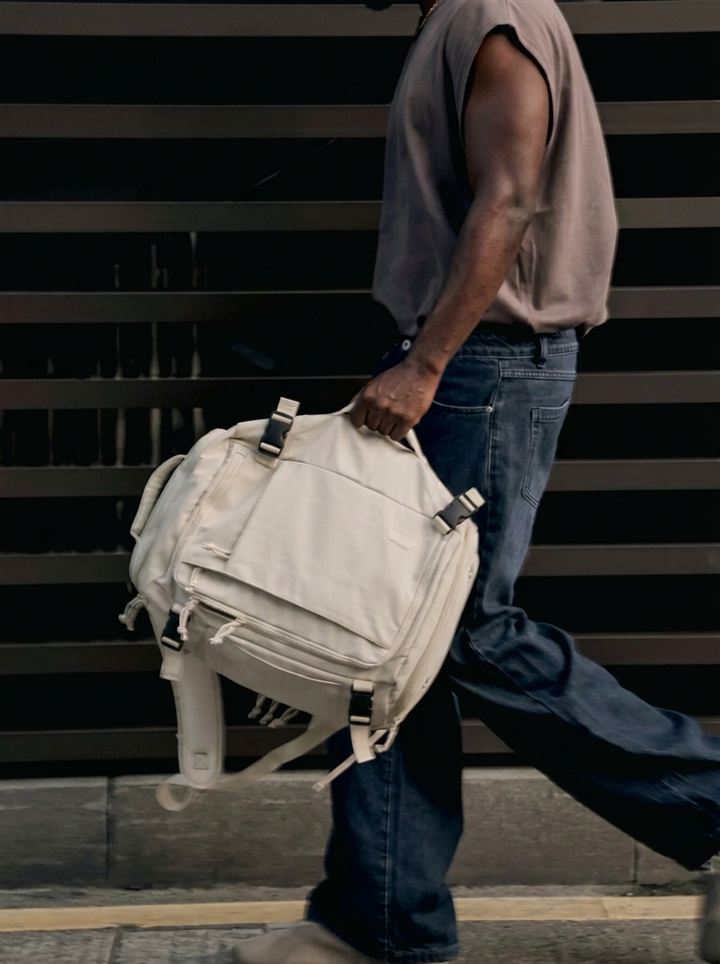 Man walking in the city carrying the cream backpack by the handle