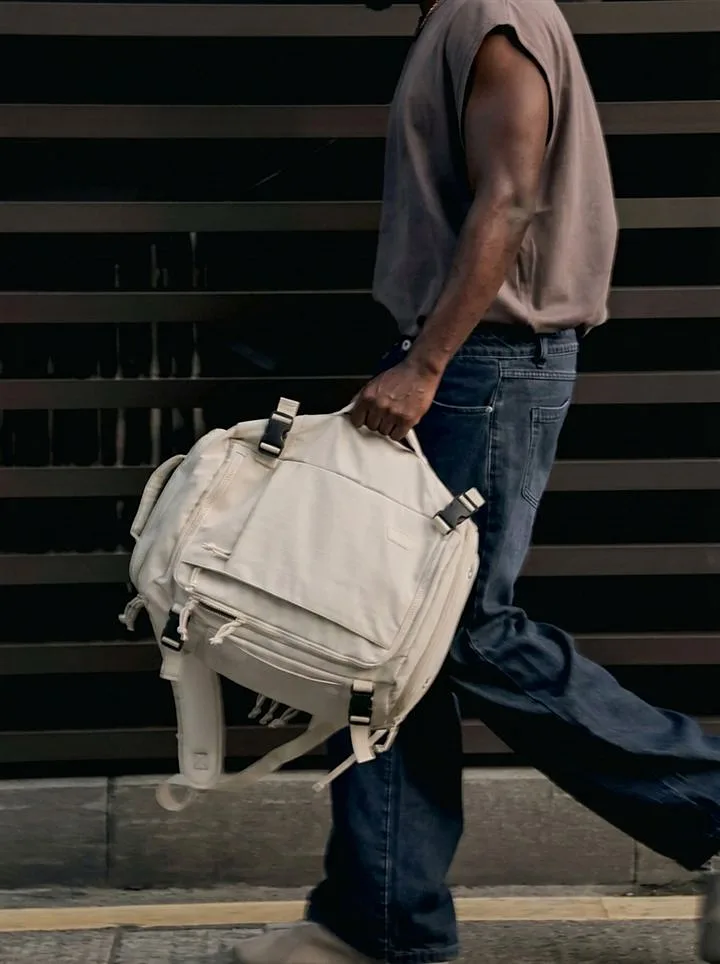 Man walking in the city carrying the cream backpack by the handle